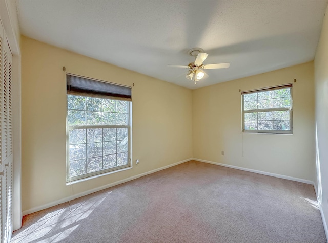 carpeted spare room featuring a healthy amount of sunlight, baseboards, and a ceiling fan