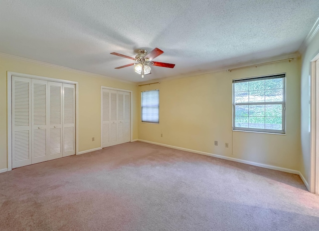 unfurnished bedroom featuring carpet, crown molding, a textured ceiling, and multiple closets