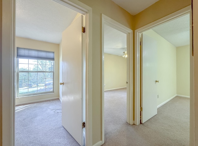 hallway with a textured ceiling, carpet flooring, and baseboards