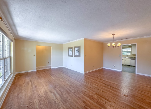 unfurnished living room featuring a textured ceiling, ornamental molding, wood finished floors, and a notable chandelier