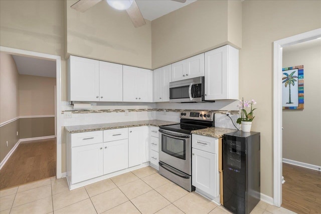 kitchen with stainless steel appliances, ceiling fan, beverage cooler, light stone counters, and white cabinetry