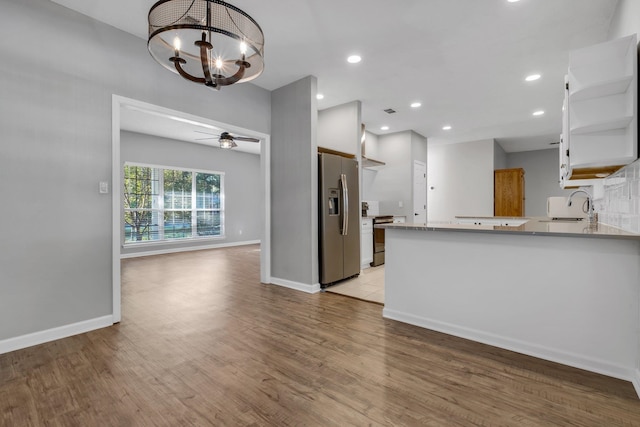 kitchen featuring ceiling fan with notable chandelier, white cabinets, light hardwood / wood-style floors, kitchen peninsula, and stainless steel appliances