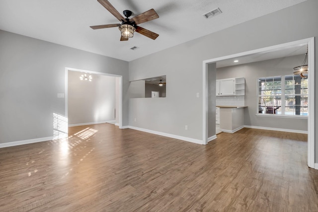 unfurnished living room featuring ceiling fan with notable chandelier and hardwood / wood-style floors