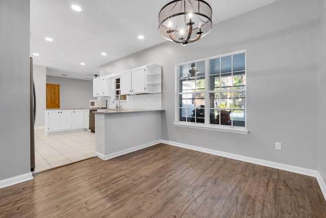 kitchen with white cabinetry, kitchen peninsula, pendant lighting, ceiling fan with notable chandelier, and decorative backsplash