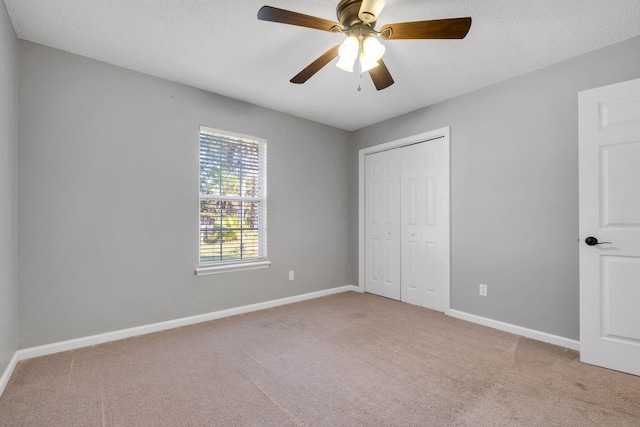 unfurnished bedroom featuring ceiling fan, light colored carpet, a closet, and a textured ceiling