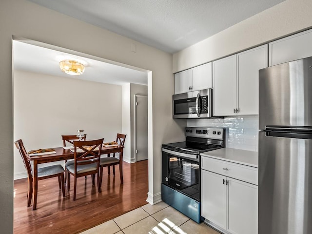 kitchen with tasteful backsplash, white cabinetry, stainless steel appliances, and light tile patterned flooring