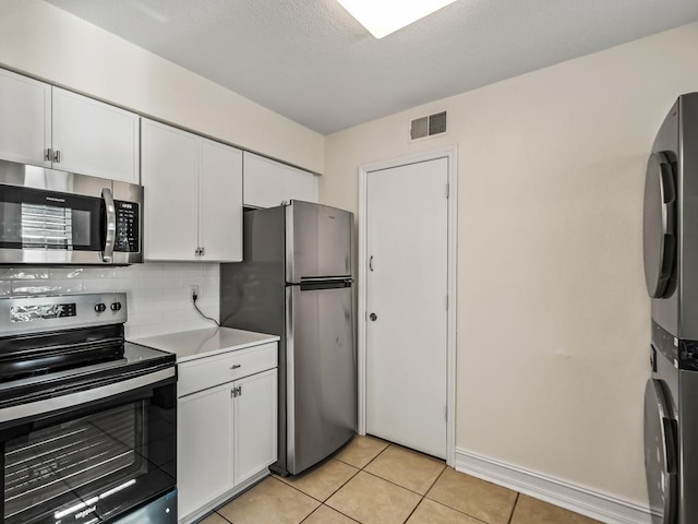 kitchen featuring stacked washer and dryer, light tile patterned floors, stainless steel appliances, decorative backsplash, and white cabinets