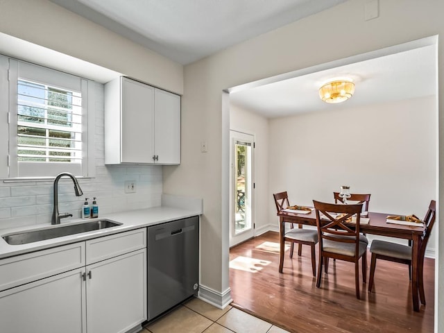 kitchen featuring white cabinetry, dishwashing machine, tasteful backsplash, light tile patterned flooring, and sink