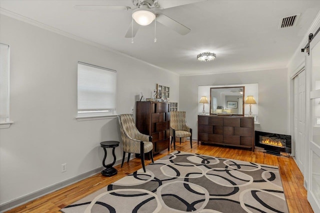 living area with ceiling fan, a barn door, crown molding, and light hardwood / wood-style flooring