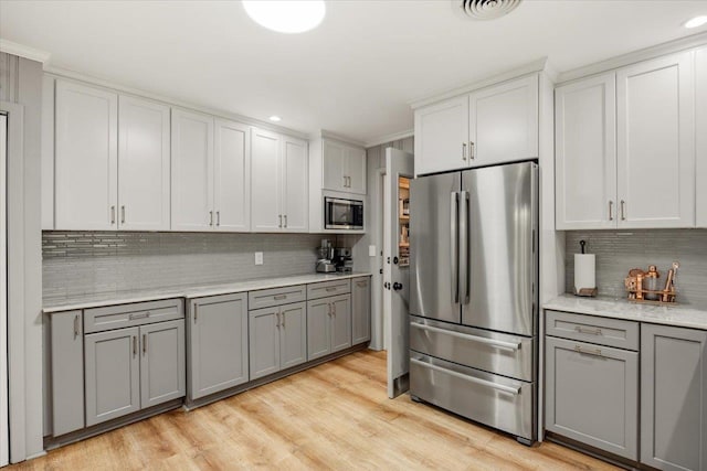 kitchen with white cabinets, light hardwood / wood-style flooring, decorative backsplash, gray cabinets, and appliances with stainless steel finishes