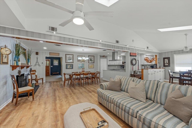 living room featuring ceiling fan with notable chandelier, light hardwood / wood-style flooring, and vaulted ceiling