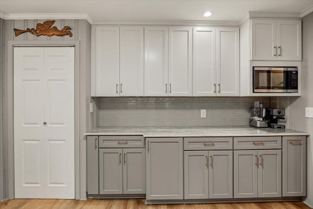 kitchen featuring light wood-type flooring, backsplash, gray cabinets, and stainless steel microwave