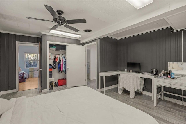 bedroom with ceiling fan, wood walls, wood-type flooring, a closet, and ornamental molding