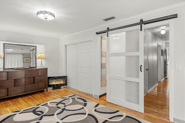 interior space with a barn door, a closet, wood-type flooring, and ornamental molding