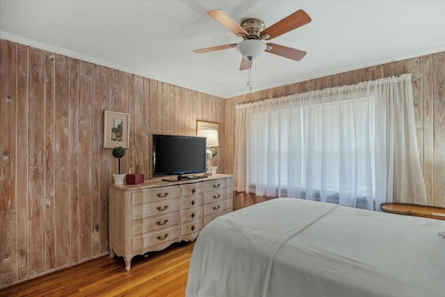 bedroom featuring ceiling fan, wood walls, light wood-type flooring, and crown molding
