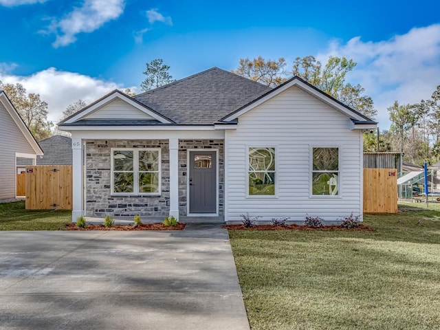 ranch-style house with stone siding, fence, roof with shingles, and a front lawn