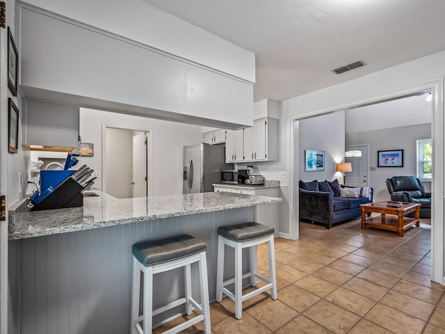 kitchen with kitchen peninsula, stainless steel fridge, a kitchen breakfast bar, light stone counters, and white cabinetry