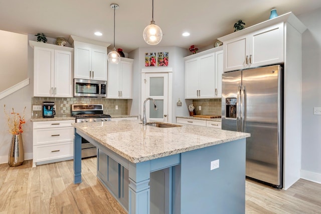 kitchen featuring appliances with stainless steel finishes, sink, white cabinets, hanging light fixtures, and a center island with sink