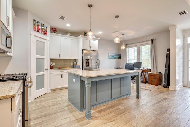 kitchen featuring appliances with stainless steel finishes, white cabinetry, hanging light fixtures, a kitchen island with sink, and light stone counters