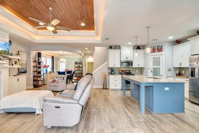 kitchen featuring stainless steel appliances, hanging light fixtures, a kitchen island with sink, and a tray ceiling