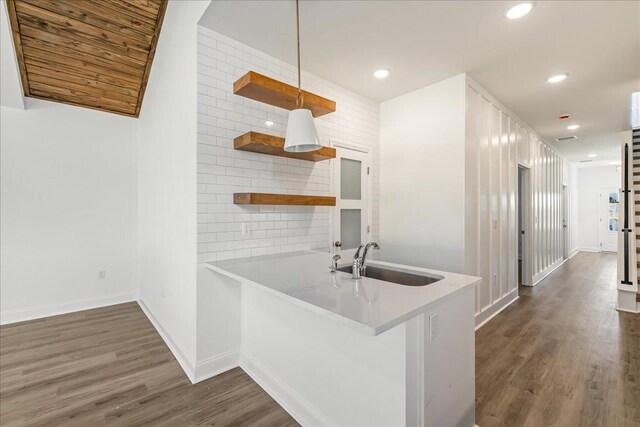 kitchen with backsplash, pendant lighting, sink, dark wood-type flooring, and kitchen peninsula