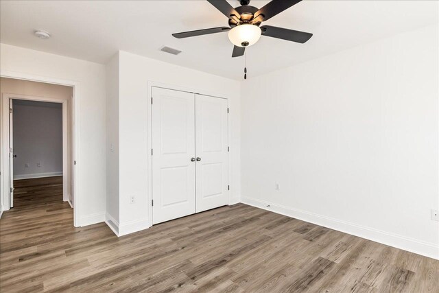 unfurnished bedroom with wood-type flooring, ceiling fan, and a closet