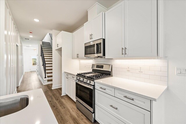 kitchen with stainless steel appliances, dark hardwood / wood-style floors, white cabinetry, and backsplash