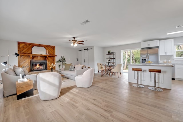 living room with a fireplace, ceiling fan, a barn door, and light wood-type flooring