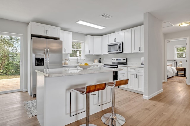 kitchen with a kitchen island, light stone counters, white cabinetry, and stainless steel appliances