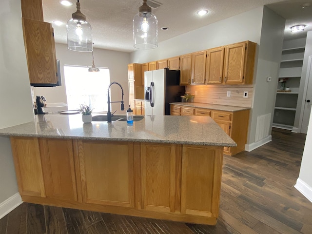 kitchen with stainless steel refrigerator with ice dispenser, sink, light stone counters, hanging light fixtures, and kitchen peninsula