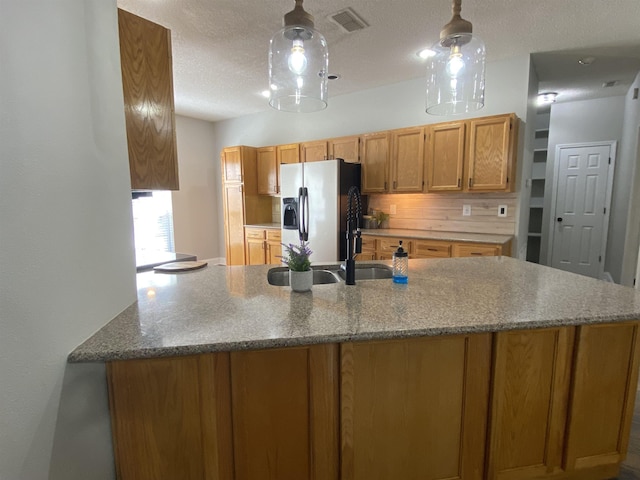 kitchen featuring stainless steel fridge, hanging light fixtures, tasteful backsplash, a textured ceiling, and kitchen peninsula