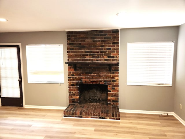unfurnished living room with a fireplace, wood finished floors, baseboards, and plenty of natural light