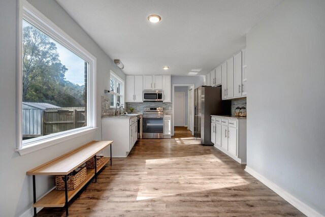 kitchen featuring light hardwood / wood-style floors, white cabinets, backsplash, and appliances with stainless steel finishes