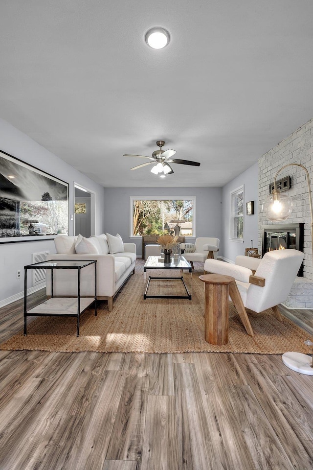 living room featuring a brick fireplace, hardwood / wood-style floors, and ceiling fan