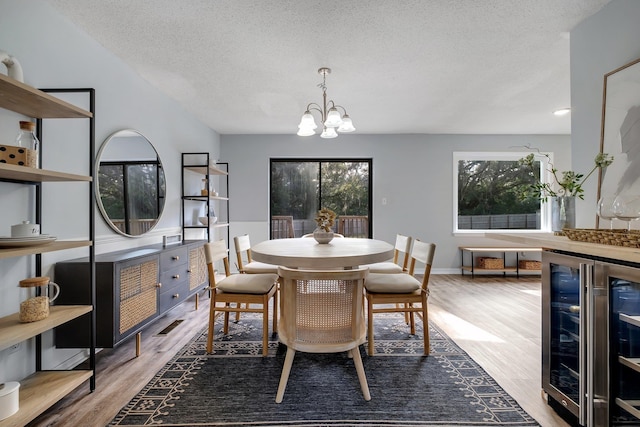 dining space featuring wood-type flooring, a textured ceiling, a notable chandelier, and wine cooler