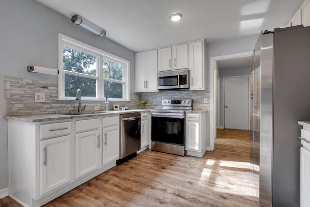 kitchen with stainless steel appliances, decorative backsplash, light wood-type flooring, white cabinets, and sink