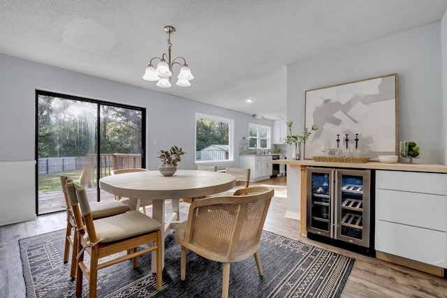 dining room featuring wood-type flooring, a notable chandelier, beverage cooler, and a textured ceiling