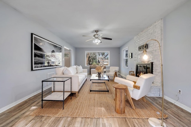 living room with hardwood / wood-style flooring, a brick fireplace, and ceiling fan