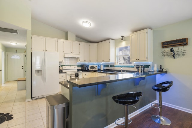 kitchen with a peninsula, white appliances, a sink, backsplash, and dark countertops