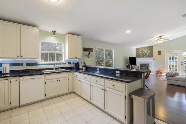 kitchen featuring a tiled fireplace, open floor plan, white dishwasher, a sink, and a peninsula