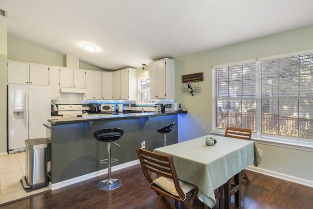 kitchen featuring dark countertops, backsplash, vaulted ceiling, white appliances, and a peninsula