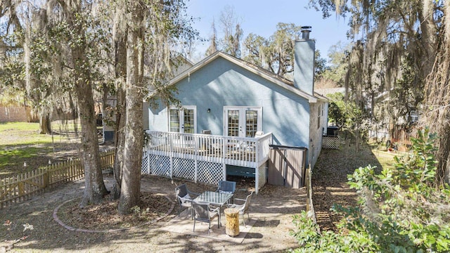 back of house with stucco siding, a chimney, fence, and french doors