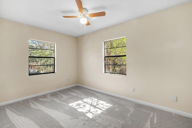 empty room featuring light carpet, a ceiling fan, baseboards, and a wealth of natural light