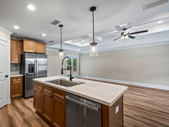 kitchen with a center island with sink, sink, crown molding, hanging light fixtures, and appliances with stainless steel finishes