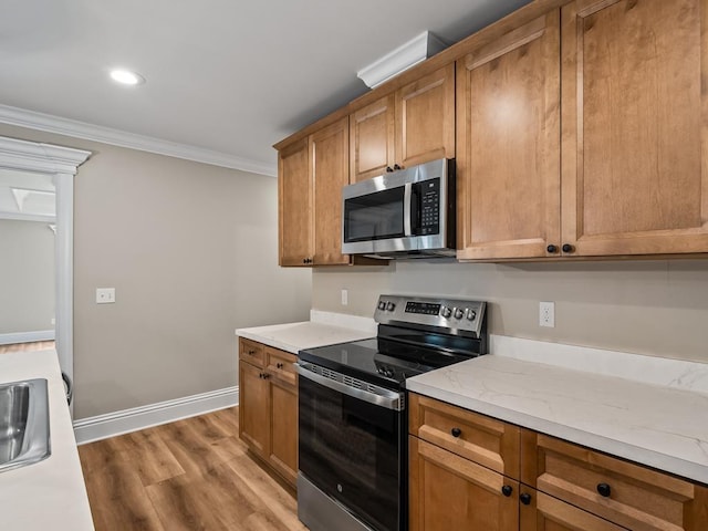 kitchen featuring light stone countertops, appliances with stainless steel finishes, sink, ornamental molding, and light hardwood / wood-style flooring