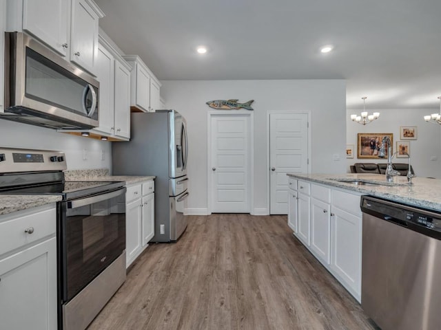 kitchen with white cabinetry, sink, stainless steel appliances, an inviting chandelier, and light stone counters