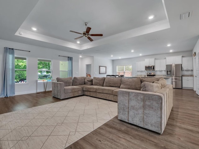 living room featuring a tray ceiling, ceiling fan, light hardwood / wood-style flooring, and ornamental molding