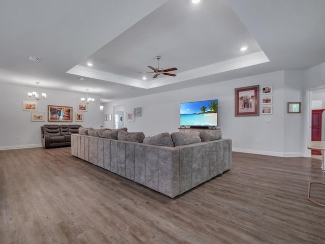 living room featuring ceiling fan with notable chandelier, dark hardwood / wood-style floors, a raised ceiling, and crown molding