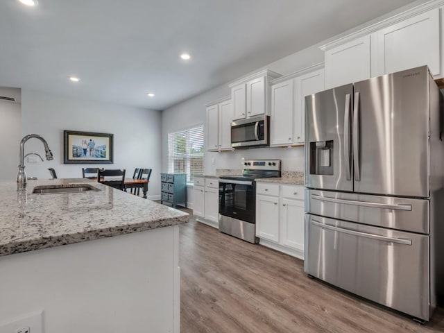 kitchen with white cabinetry, sink, stainless steel appliances, light stone counters, and light hardwood / wood-style flooring