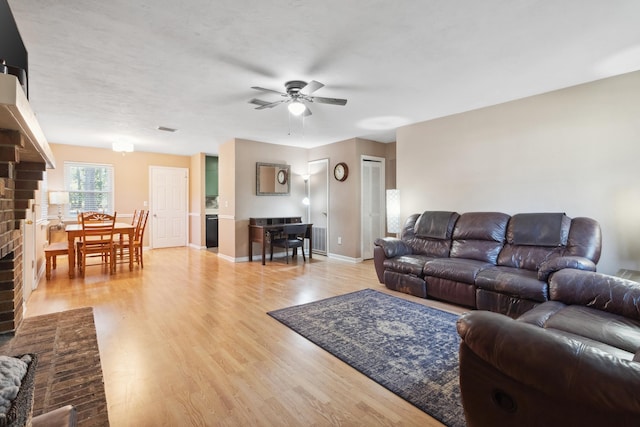 living area featuring light wood-style floors, a fireplace, baseboards, and a ceiling fan